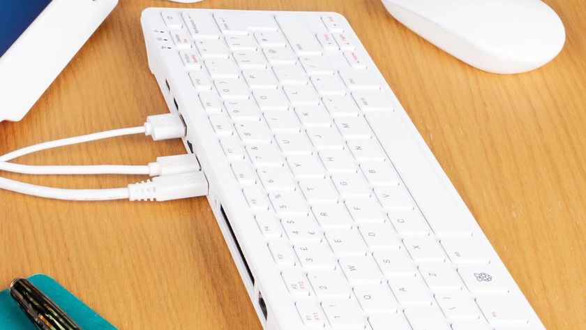 A promotional image of a Raspberry Pi 500 computer on a desk, with various cables attached to its rear ports