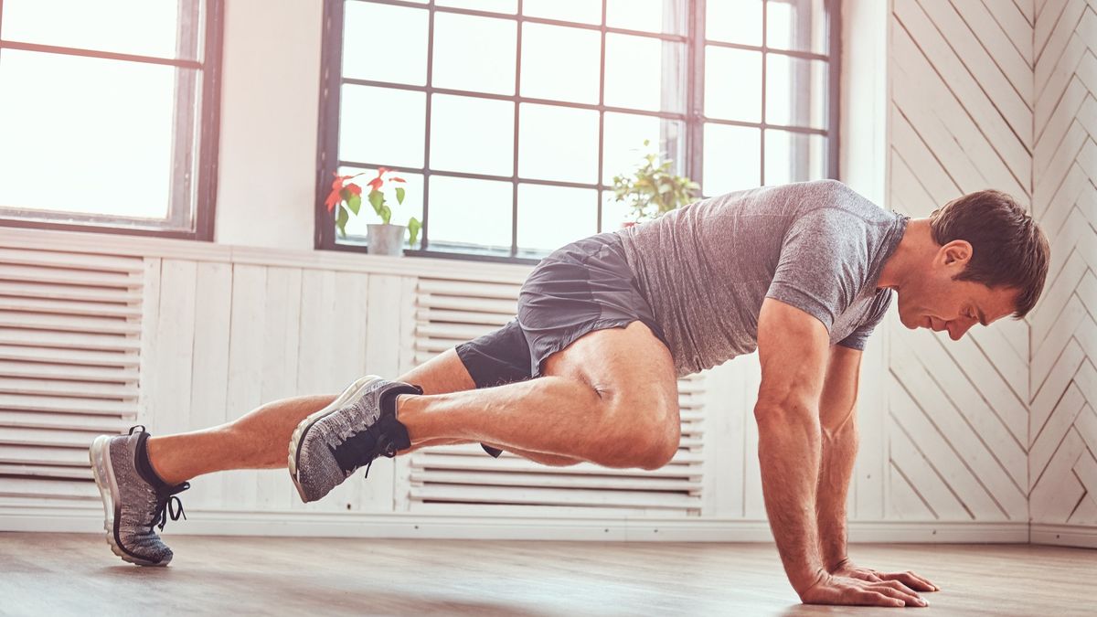 Man in light and airy studio performing a spiderman plank with right knee tapping right elbow