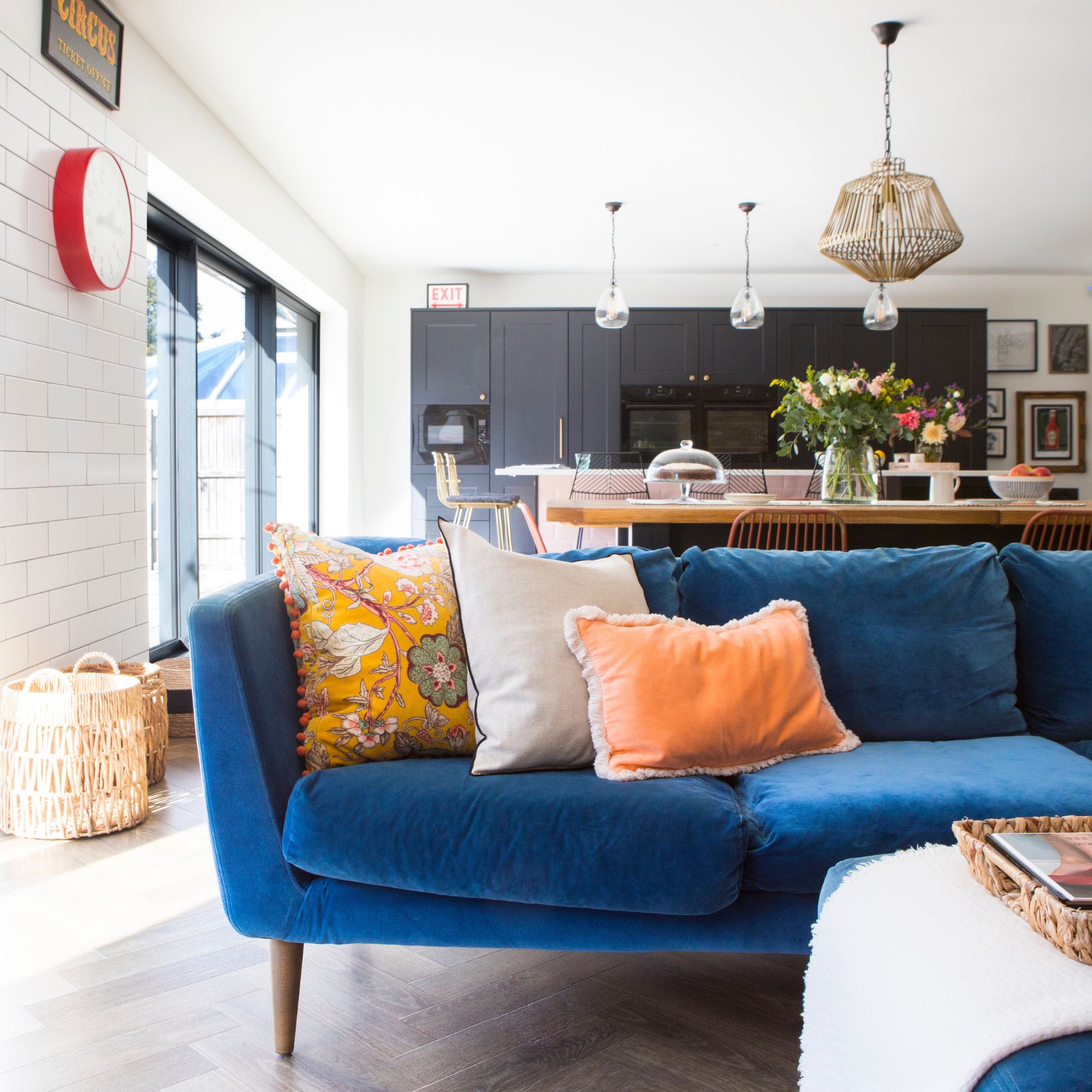 Open plan kitchen and living space with a kitchen in the background and a blue sofa with colourful cushions on it in the foreground