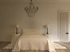 a white bedroom with side tables covered in sheets with a decorative chandelier and limewash walls