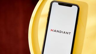 Mandiant logo on a smartphone which laid down flat on a circular wood tray, which itself is placed on top of a dark oak table