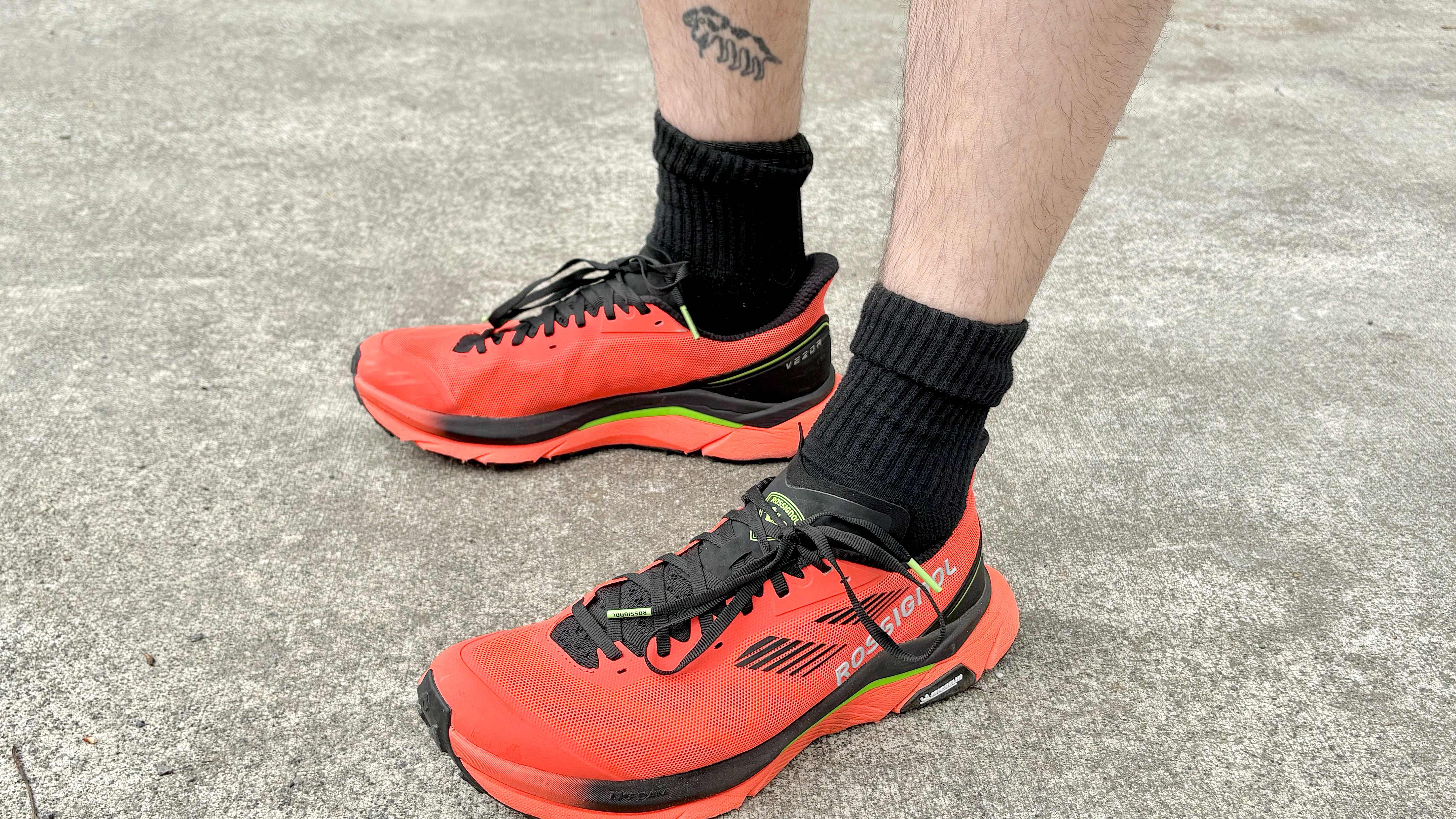 Close-up of the Rossignol Vezor trail running shoes in bright red/orange next to the Garmin Forerunner 570 smartwatch