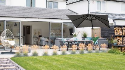 A contemporary patio at the back of a white and gray home. With ornamental grasses framing the edge of the patio