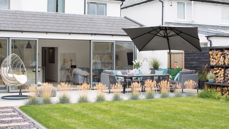 A contemporary patio at the back of a white and gray home. With ornamental grasses framing the edge of the patio