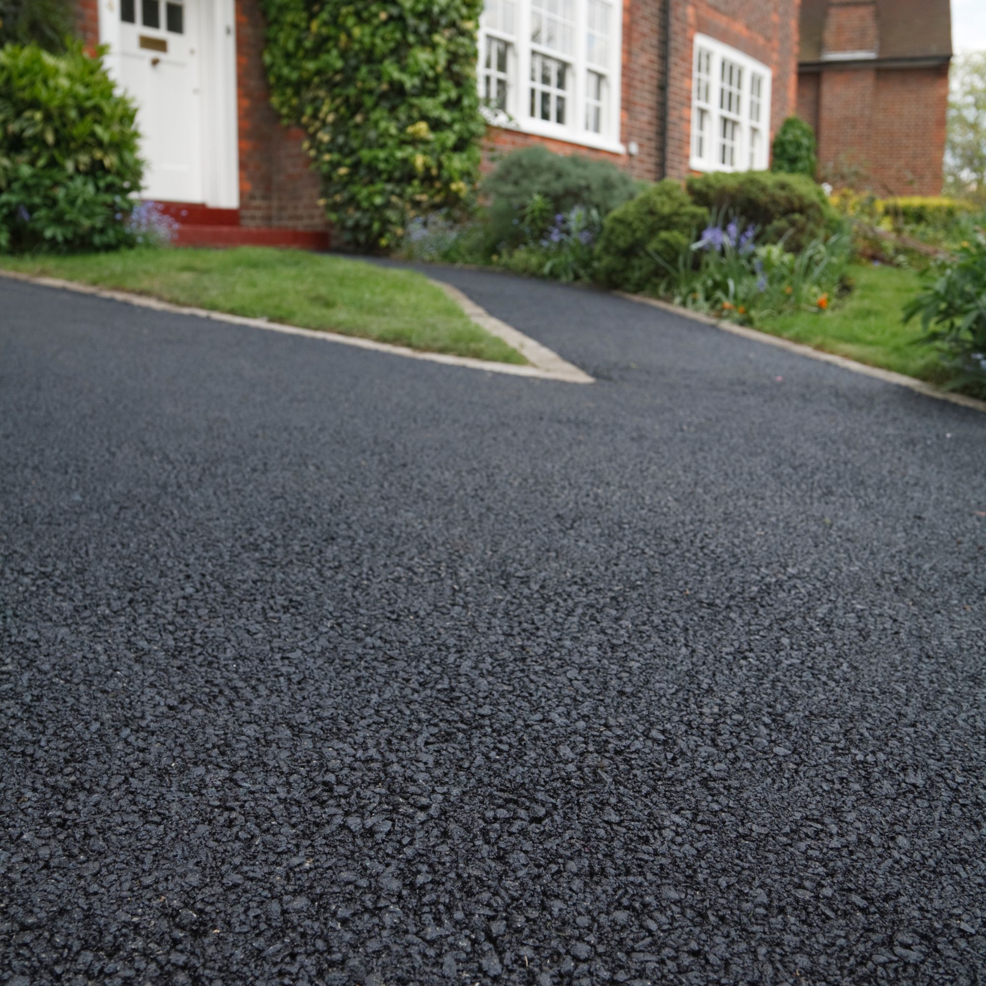 Close up of a tarmac driveway and path leading to the front door of brick home