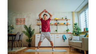 Man doing a star jump on a yoga mat at home.