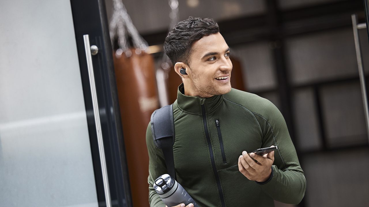 A man leaving the gym carrying a water bottle and wearing the Jabra Elite 4 Active