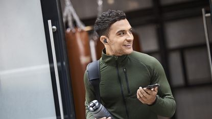 A man leaving the gym carrying a water bottle and wearing the Jabra Elite 4 Active