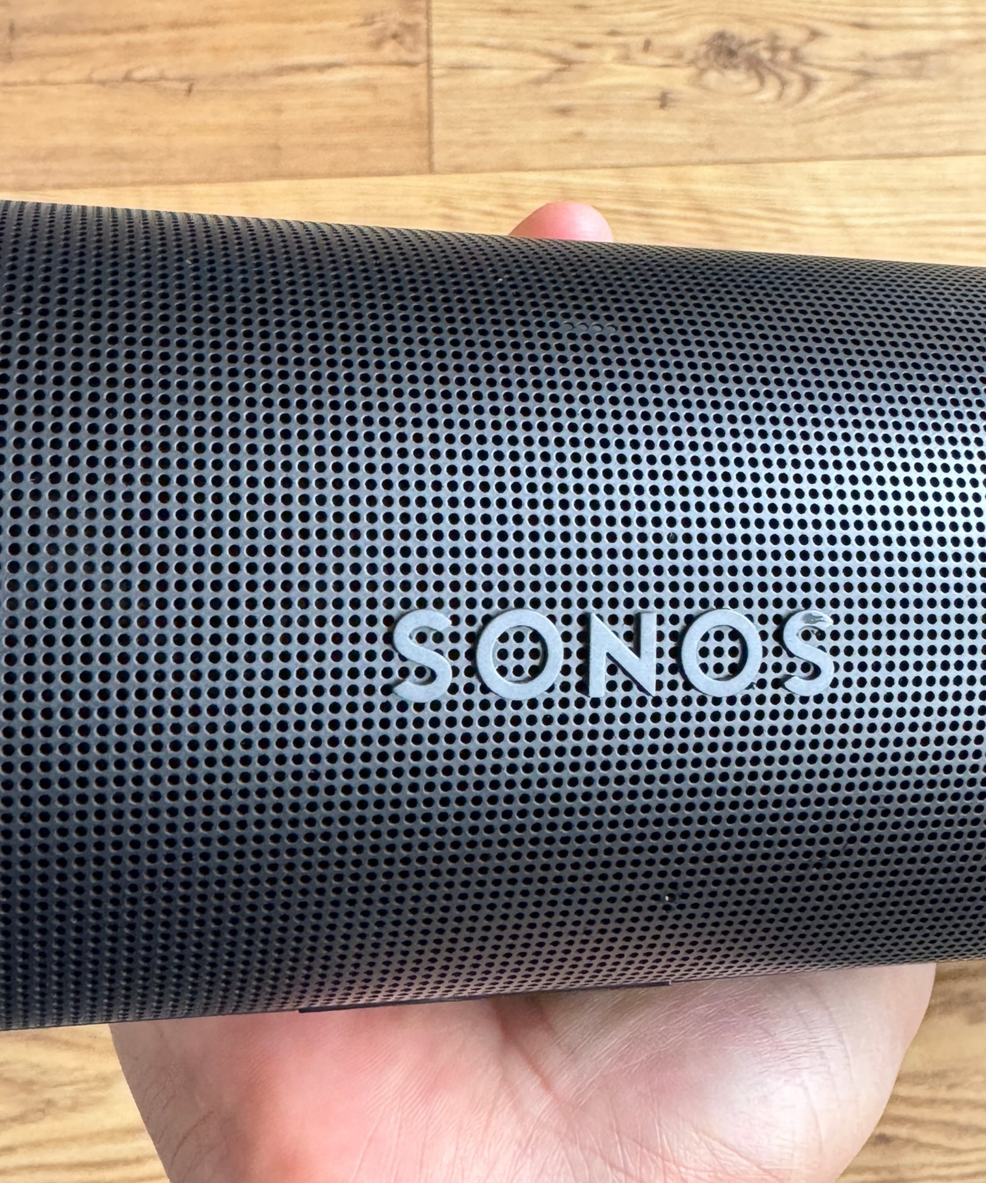 Sonos Arc soundbar held in hand above wooden floor.