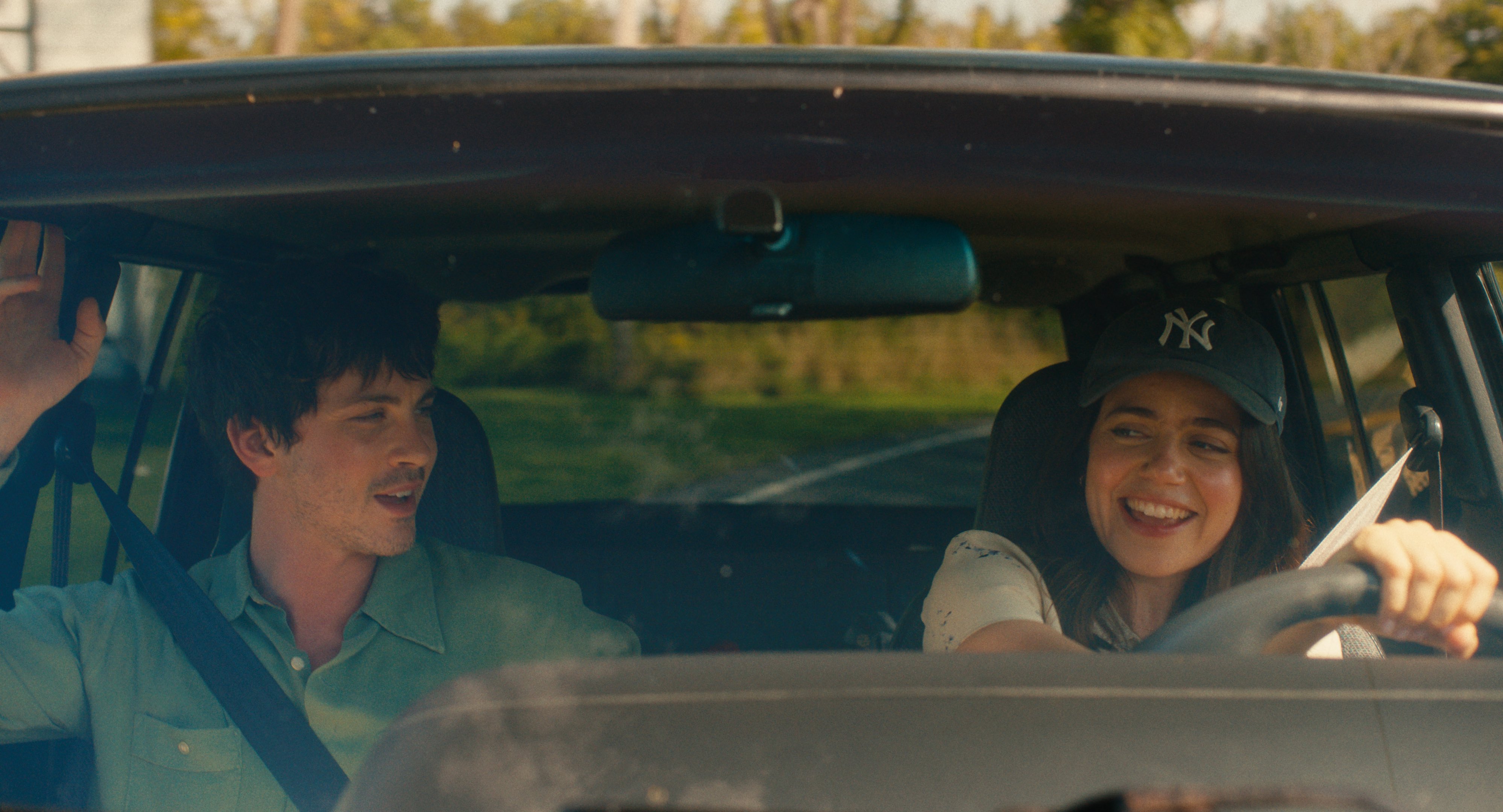 logan lerman and molly gordon as isaac and iris driving in a car in a still from the movie oh hi