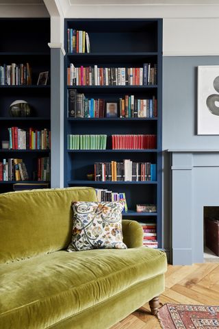 A living room with a yellow sofa and blue bookshelf