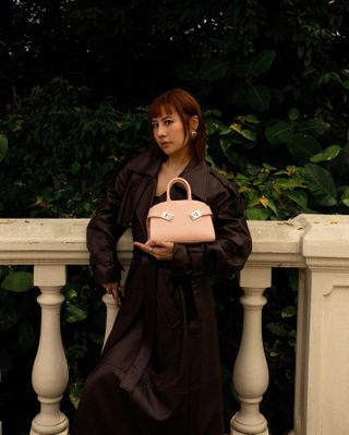 Woman wears brown trench coat and carries small beige bag