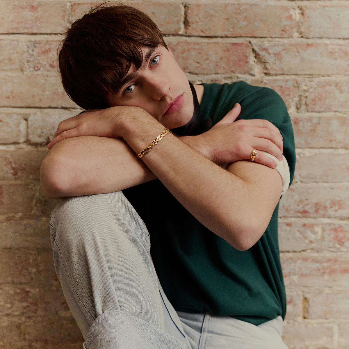 Promo image of Spike Fearn for his December In Focus feature. He is sitting leaning on his knee with his face resting on his hands. He is wearing a green Dior t-shirt with the sleeves rolled up and light wash denim.