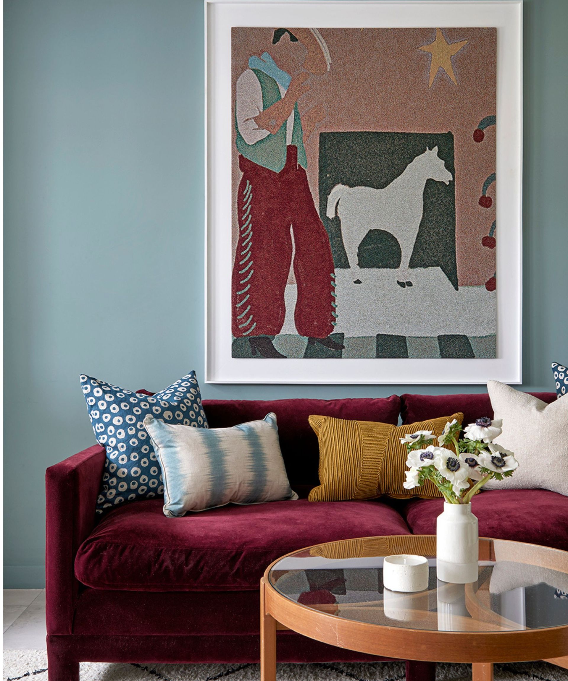 living room with blue wall, purple velvet sofa and colorful artwork and cushions