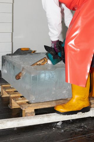 Person in wellies carves ice block with chain saw