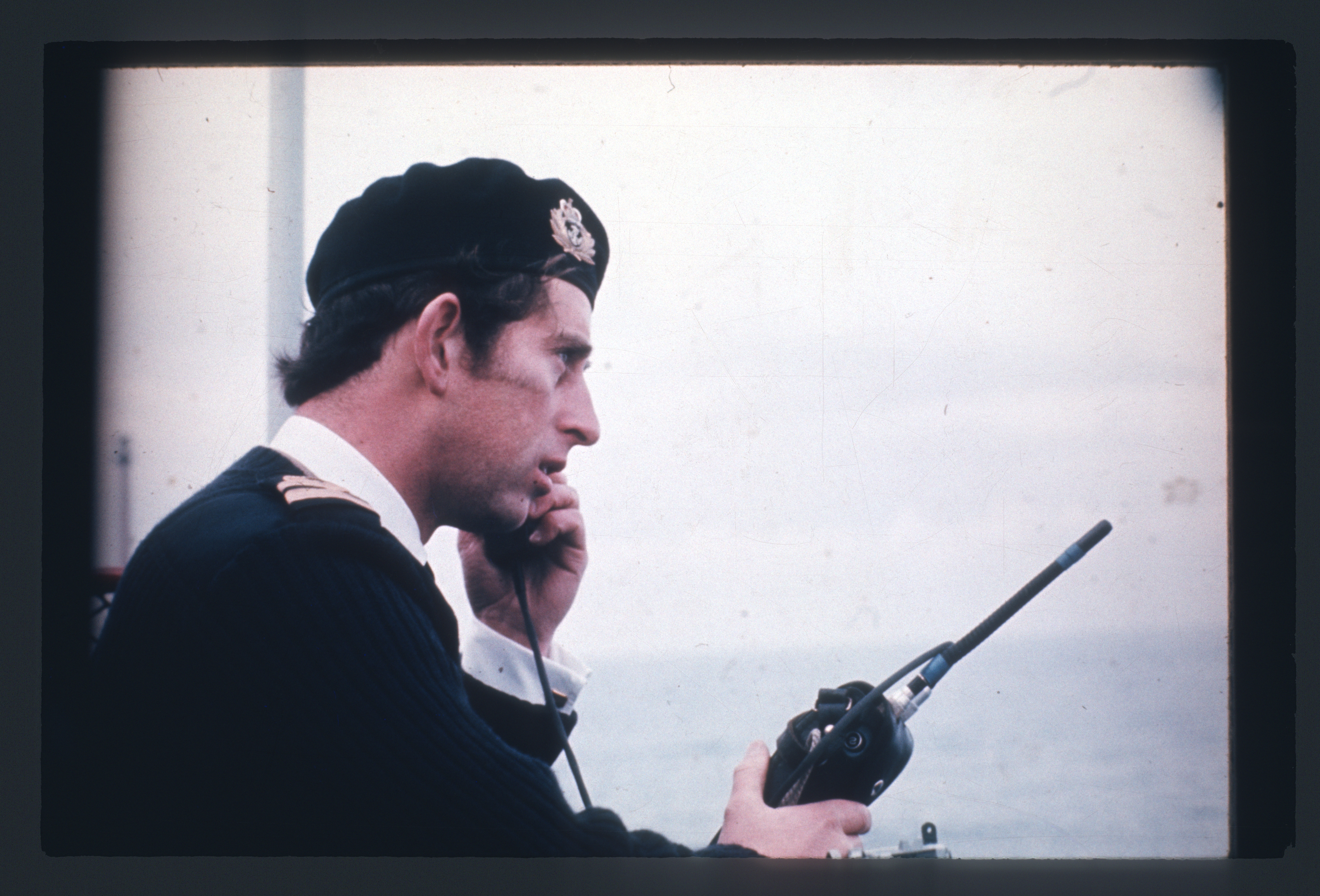 Prince Charles speaking on a walkie talkie in a naval uniform