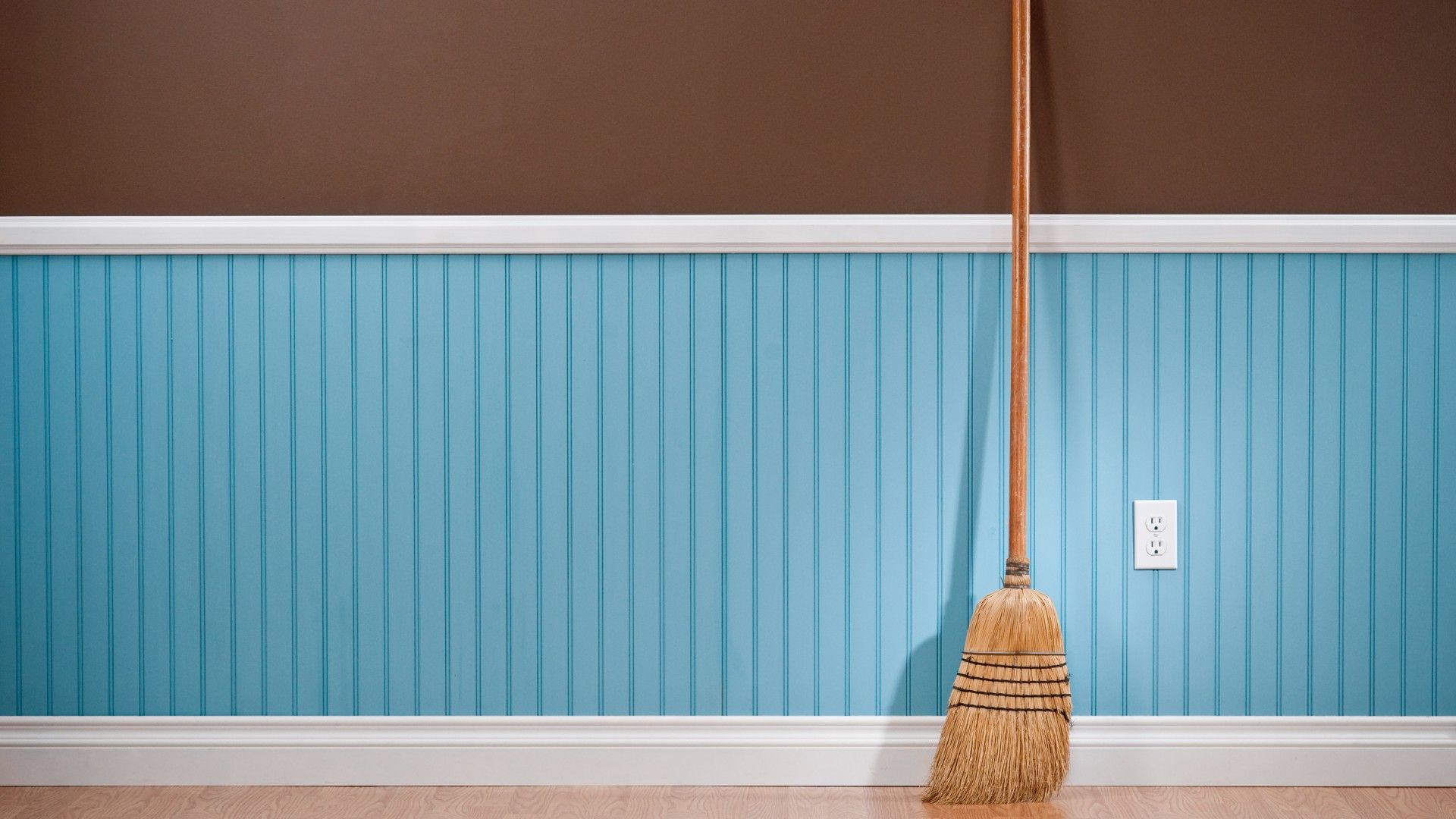 Room with blue walls and paneling with a broom to suggest how to clean skirting boards