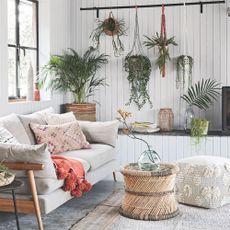 A grey living area with hanging plants, rattan features and colourful cushions