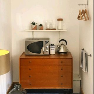 Small kitchen set up for an Airbnb property with a microwave and kettle on a vintage chest of drawers