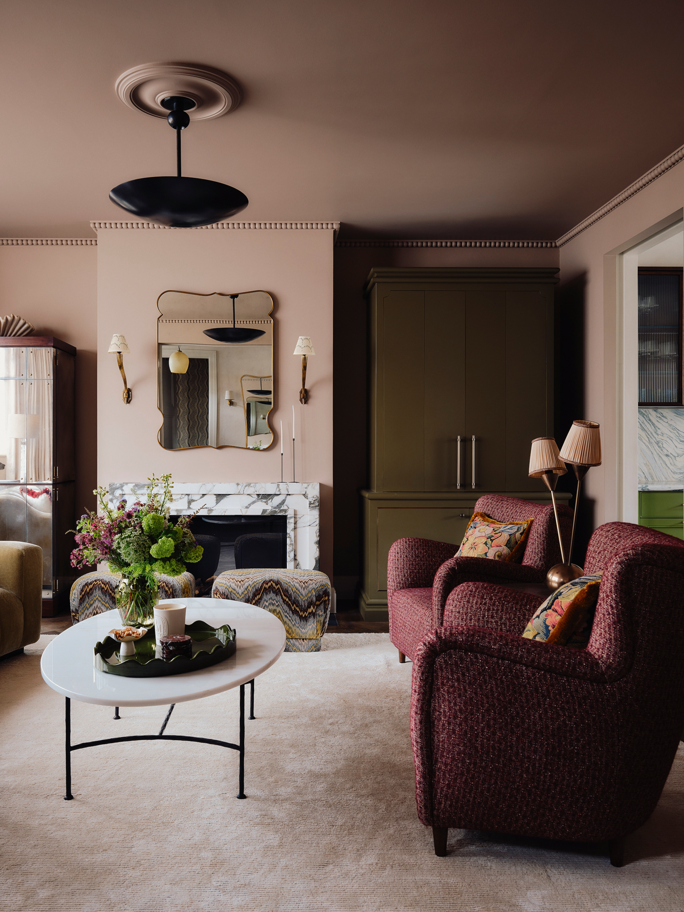 Pink living room with burgundy armchairs, white stone coffee table, white stone fireplace and embroidered footstool