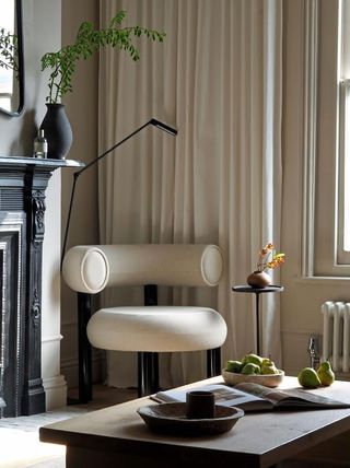 a corner of a living room with a modern chair, coffee table and light next to floor-length beige curtains