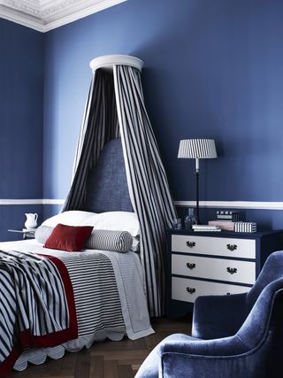 Blue bedroom with stripy bedhead curtain and bedsheets, blue velvet armchair