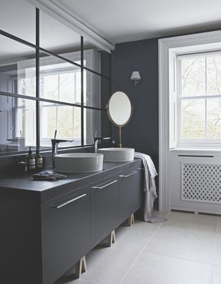 A gray bathroom with gray cabinets and an off-white tile floor. There are two sinks on the counter and a mirror wall