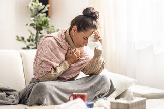 A woman sits up in bed holding a tissue in one hand and her head on the other