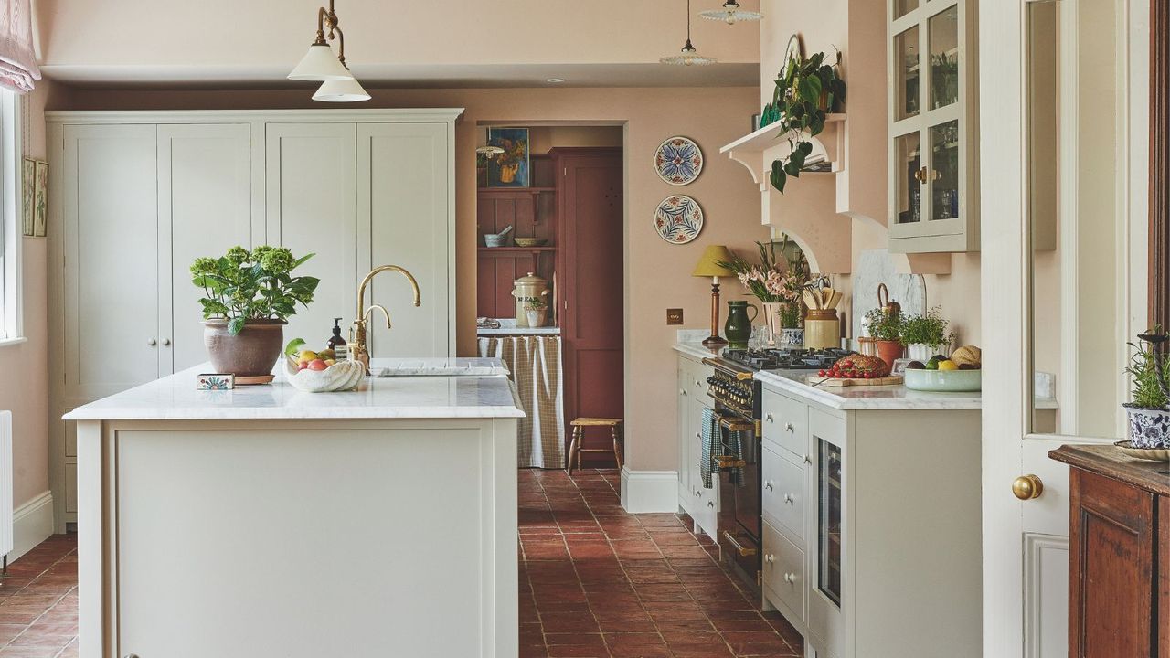 A rustic country style kitchen with light painted cabinets and island, and white countertops. Pink painted walls. 