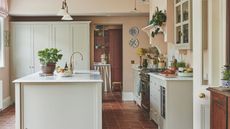 A rustic country style kitchen with light painted cabinets and island, and white countertops. Pink painted walls.
