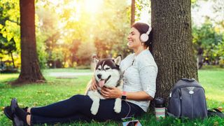 Woman with headphones on sitting in the grass with dog