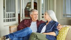 Mature good looking couple talking while sitting on sofa at home