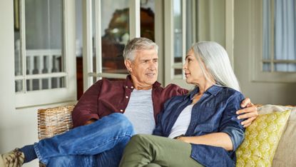 Mature good looking couple talking while sitting on sofa at home