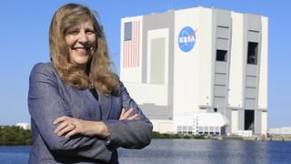 a woman standing in front of a square-shaped building that has an american flag and a nasa logo on the side