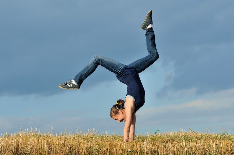 A teen girl does a handstand in a meadow.