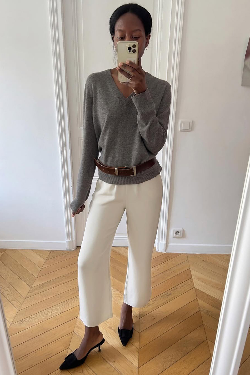 a woman wearing a gray v neck sweater, white cropped pants, and black mule heels