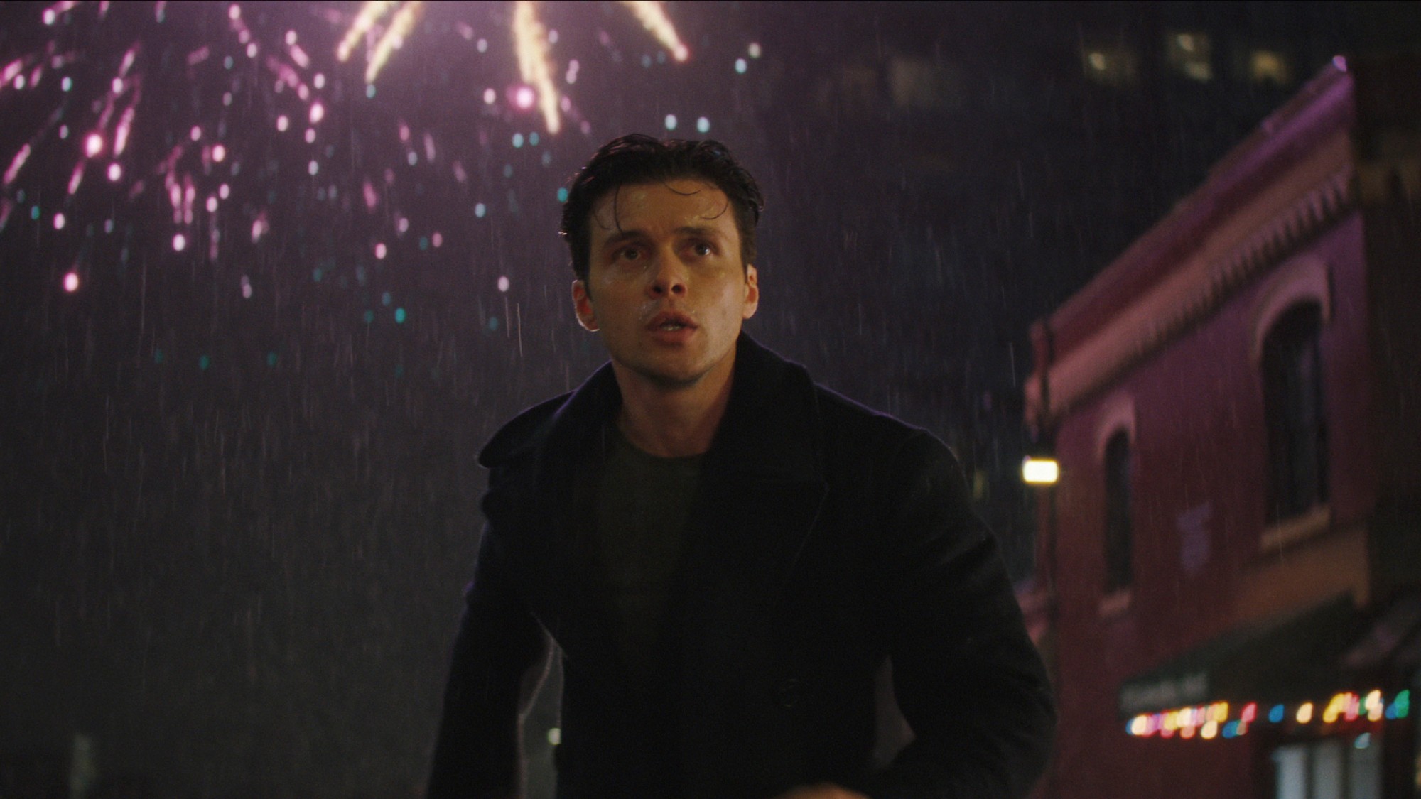 Nick Robinson running through the rain while fireworks go off behind him.