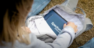 Young woman opening a backpack with a notebook that says "Spectrum Scholars"