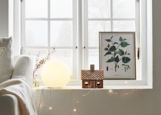 A globe lamp lit up by a window besides some fairy lights and a framed print