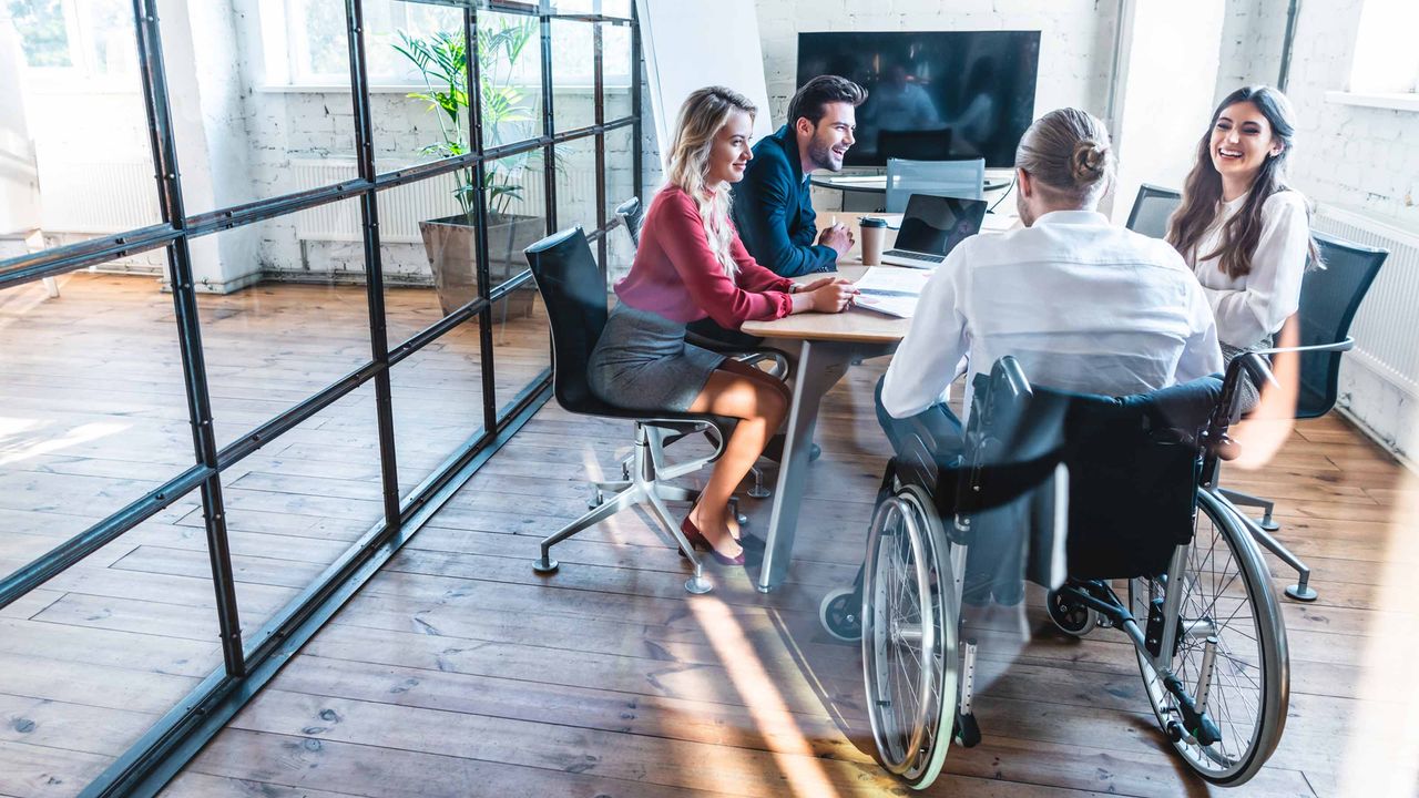 Workers sit at a conference room table. One man at the table is in a wheelchair.