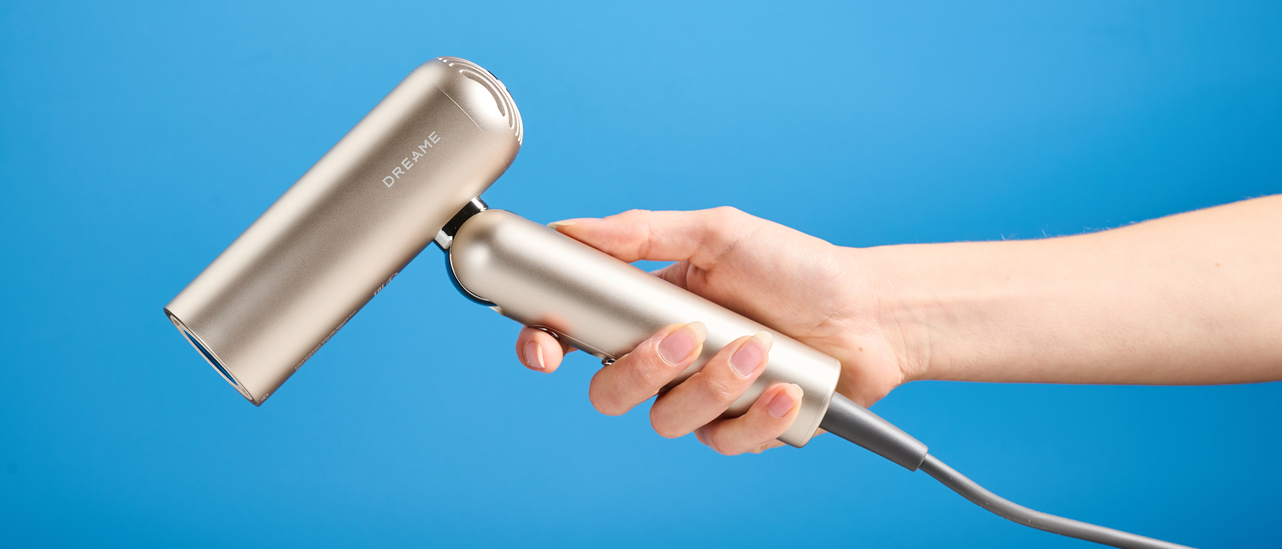 A hand holding the Dreame Pocket Neo in gold photographed in front of a blue background.