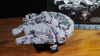 Lego Millennium Falcon set on a stand in front of the set's box, all on a wooden table