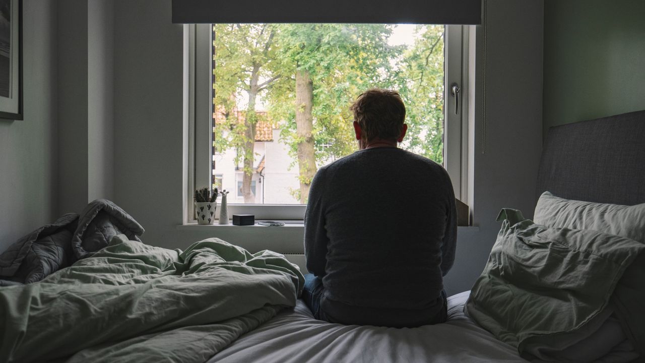 A man sitting on his bed looking out of a window