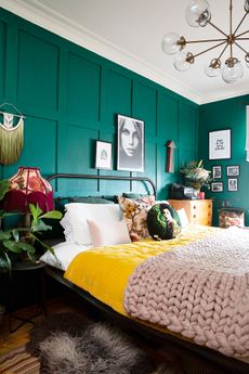 Green panelled walls in a master bedroom with a metal bed, yellow and pink throws, and patterned cushions