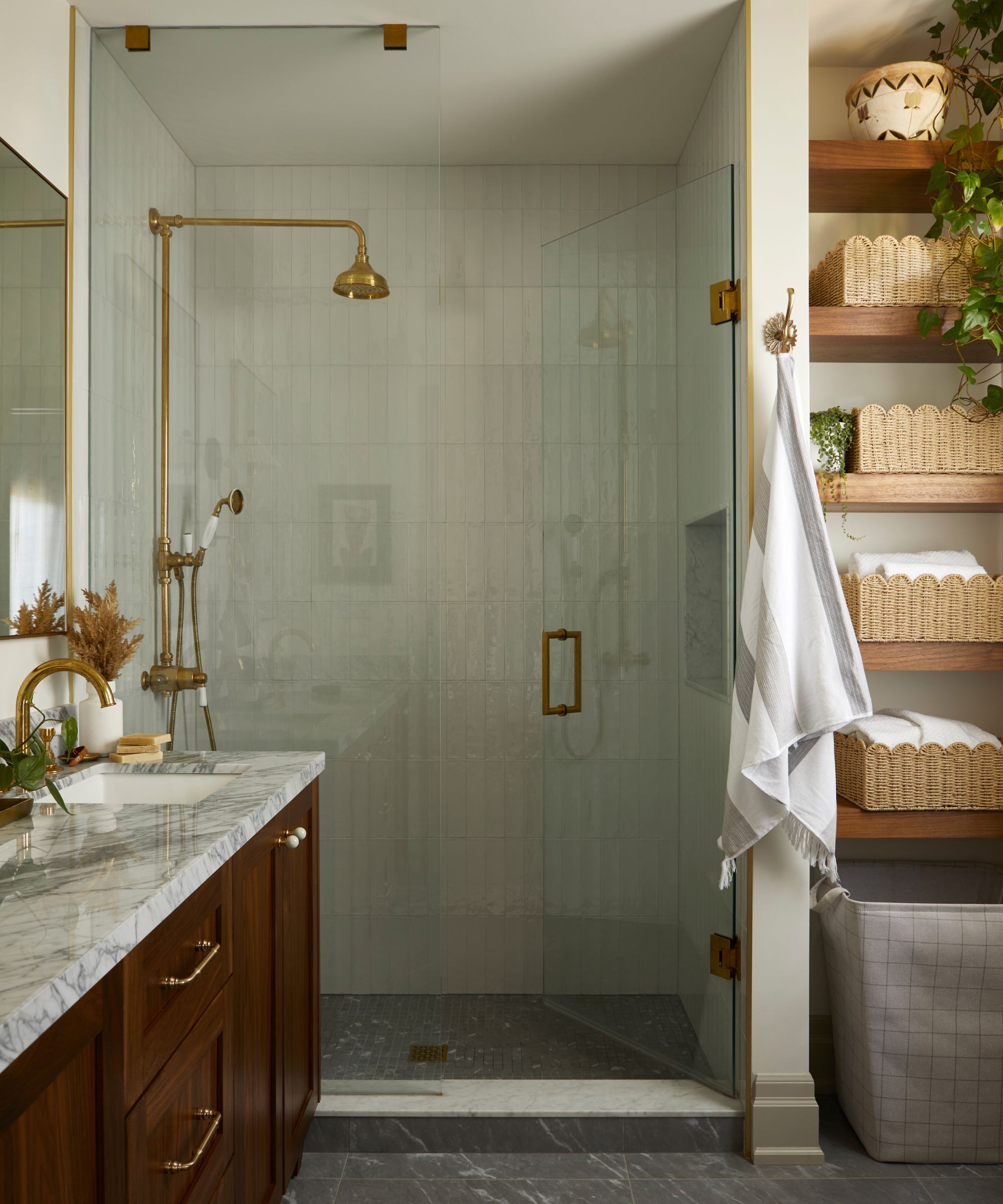 a warm neutral ensuite bathroom with a dark wooden floating vanity with marble top, shower enclosure, and wooden floating shelves