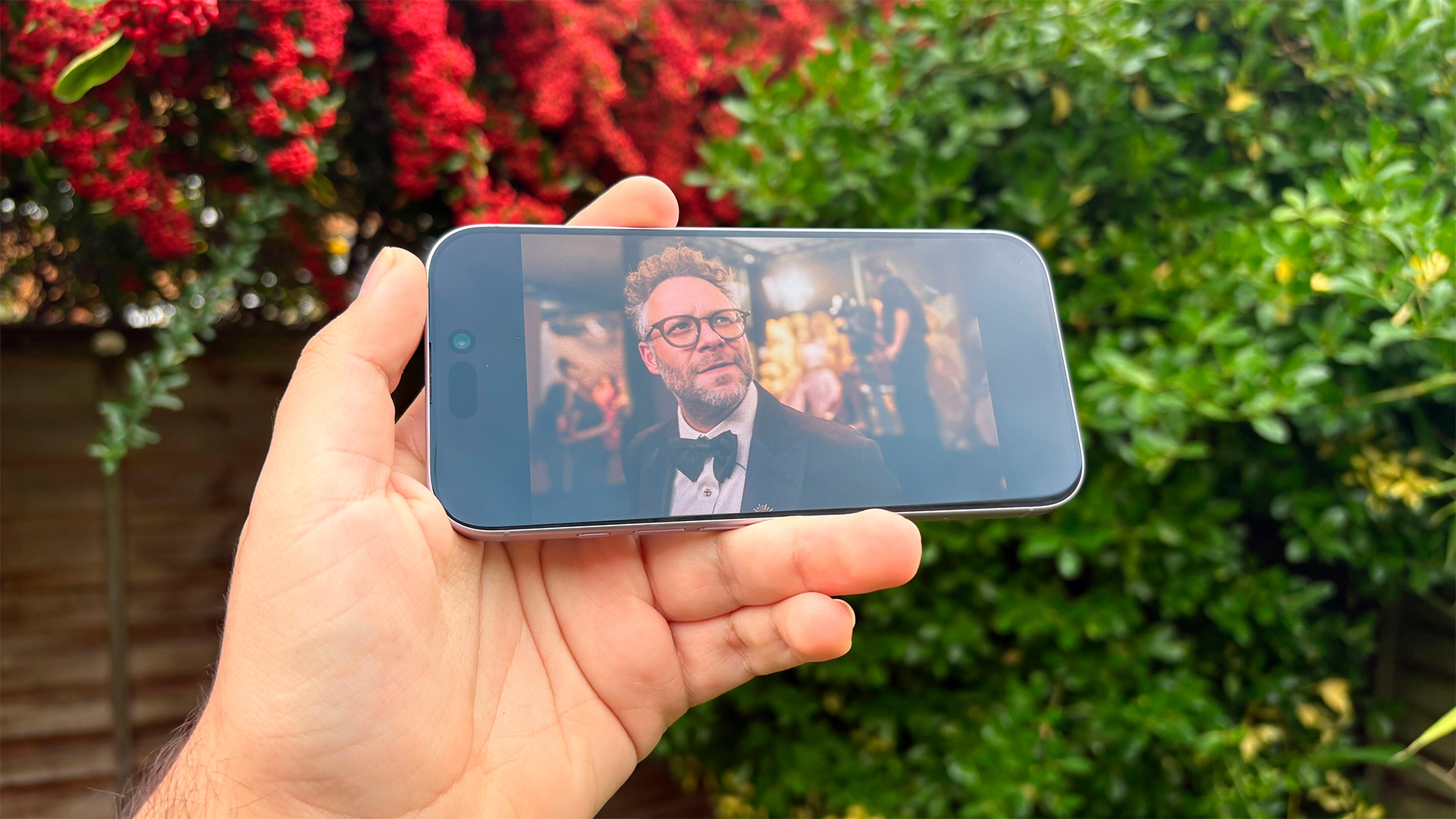 Apple iPhone 17 smartphone held in hand in front of bushes, on screen is The Studio