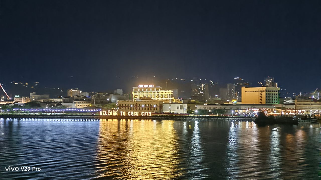 A vibrant city skyline at night reflecting its lights on the water, creating a mesmerizing view