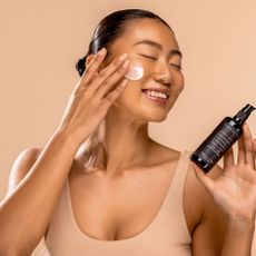 Woman putting skincare on her face with beige background