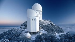 kitt peak national observatory on a tall mountaintop with a dusting of snow on the ground and three large structures two tall white structures and one small dome.