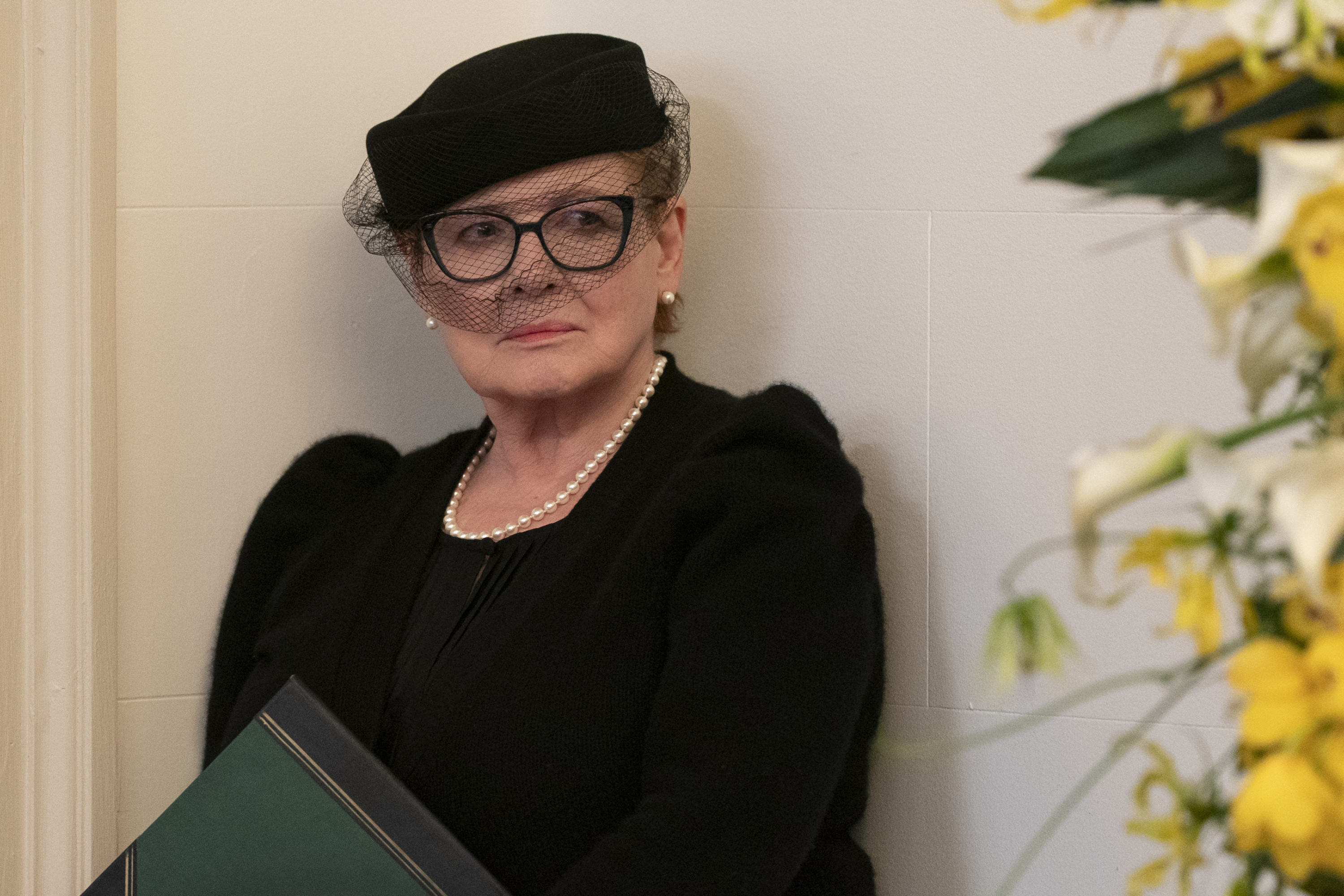 Dianne Wiest as Lorraine Coluca, wearing a funeral outfit with a black veil and holding a ledger, in &#039;Only Murders in the Building&#039; season 5.